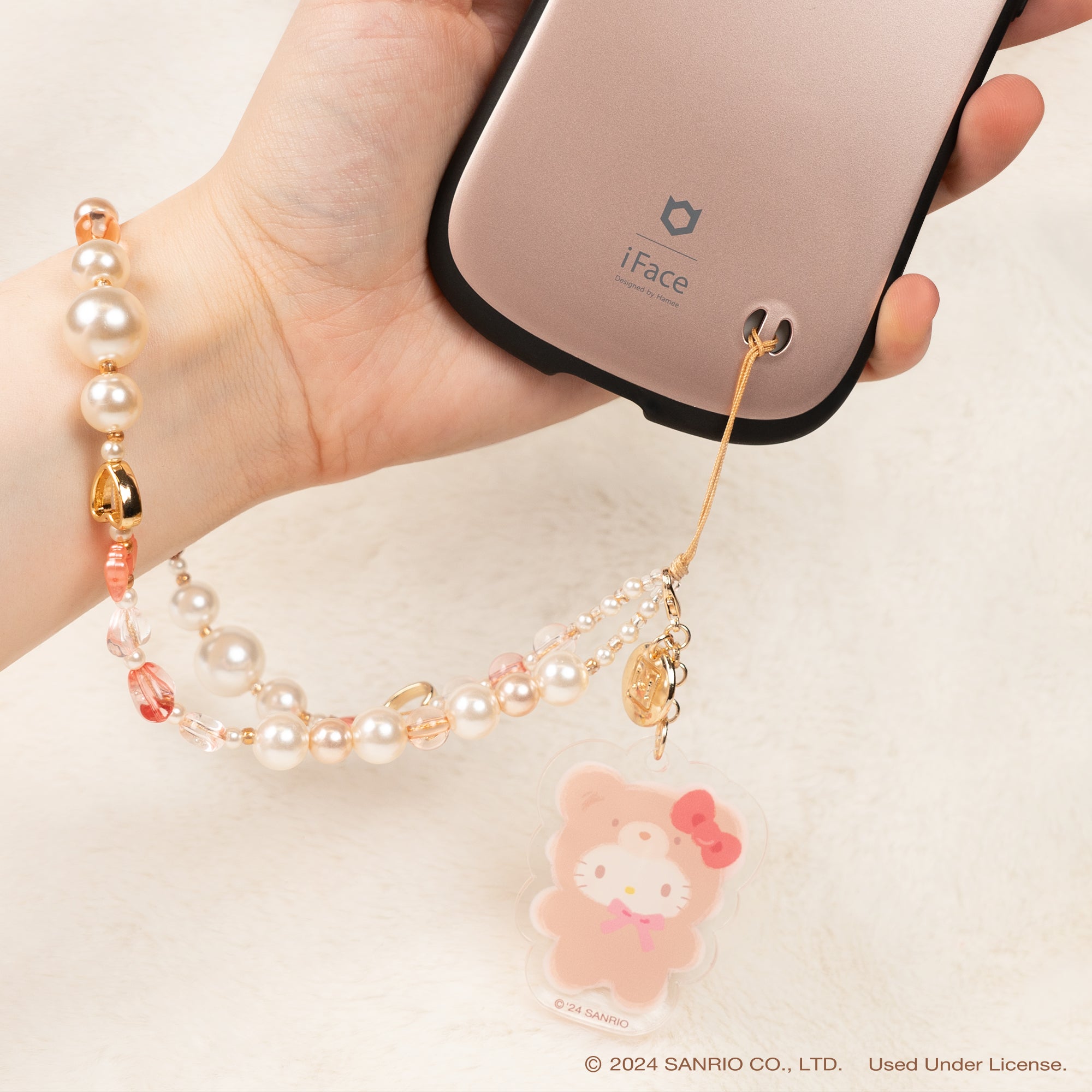 Person using the Hello Kitty phone strap while shopping outdoors.